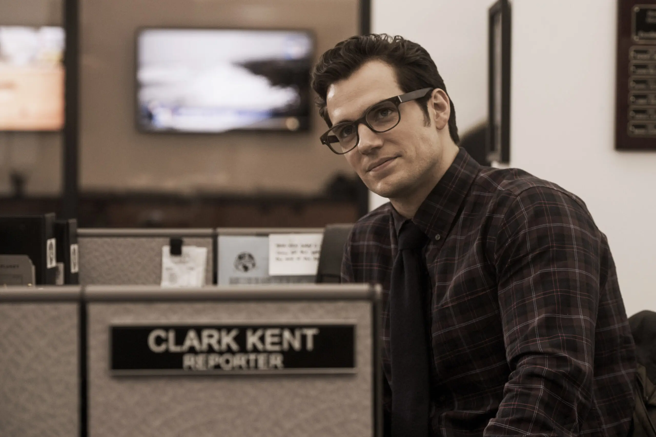 Clark Kent sitting in his cubicle where he's a reporter by day.