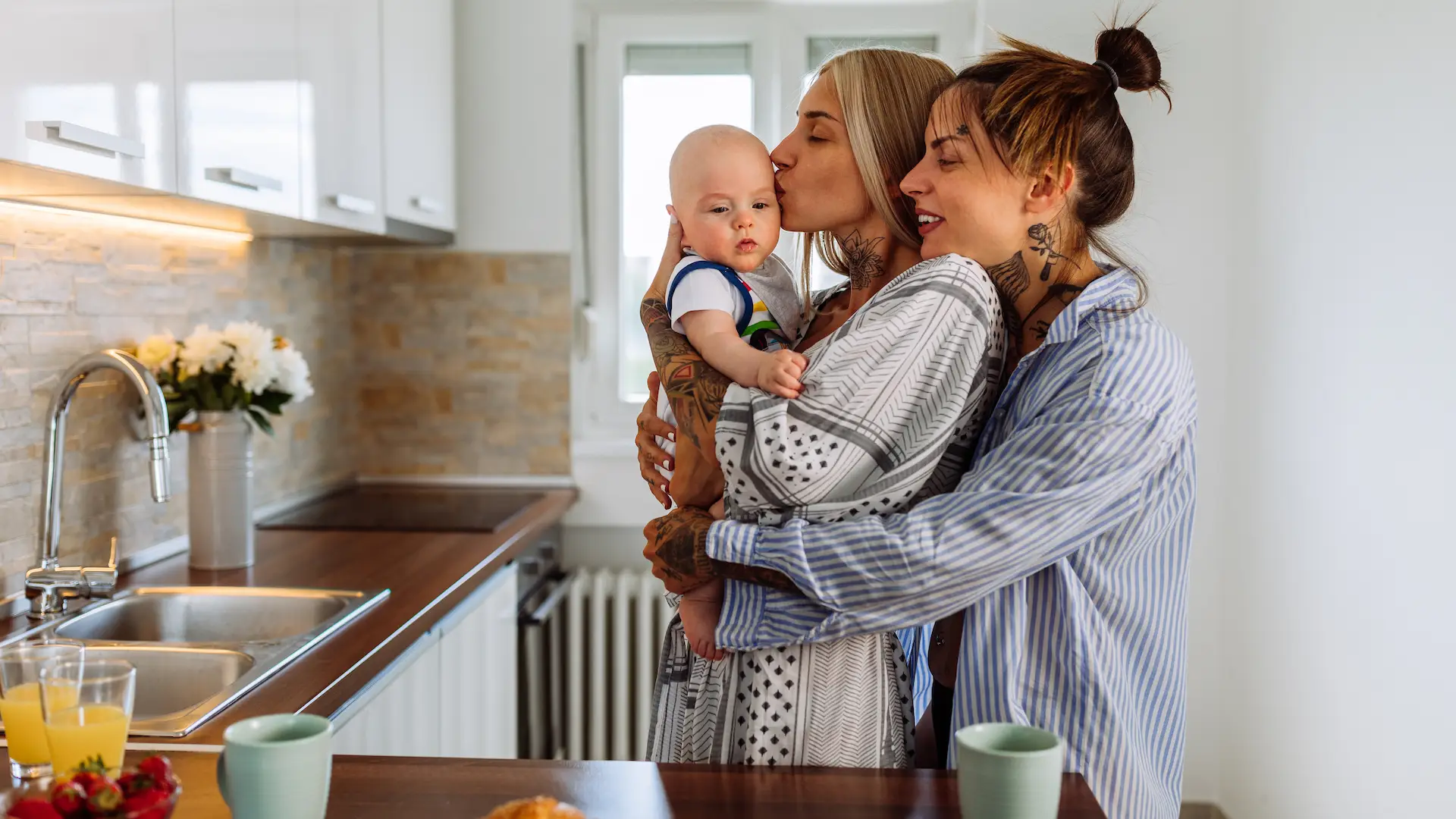 Same sex couple in pajamas hold their baby son and enjoying time spent together at home
