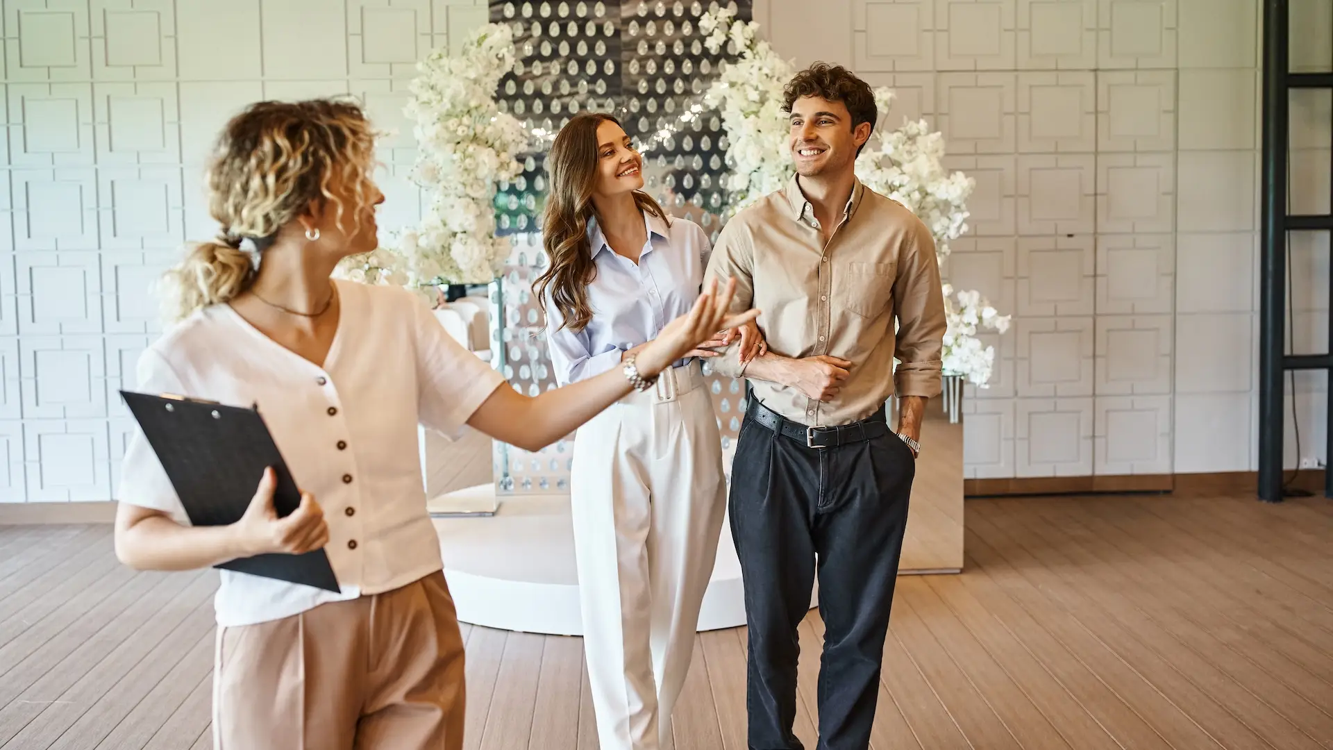 professional event manager with clipboard showing wedding venue with floral decor to happy couple