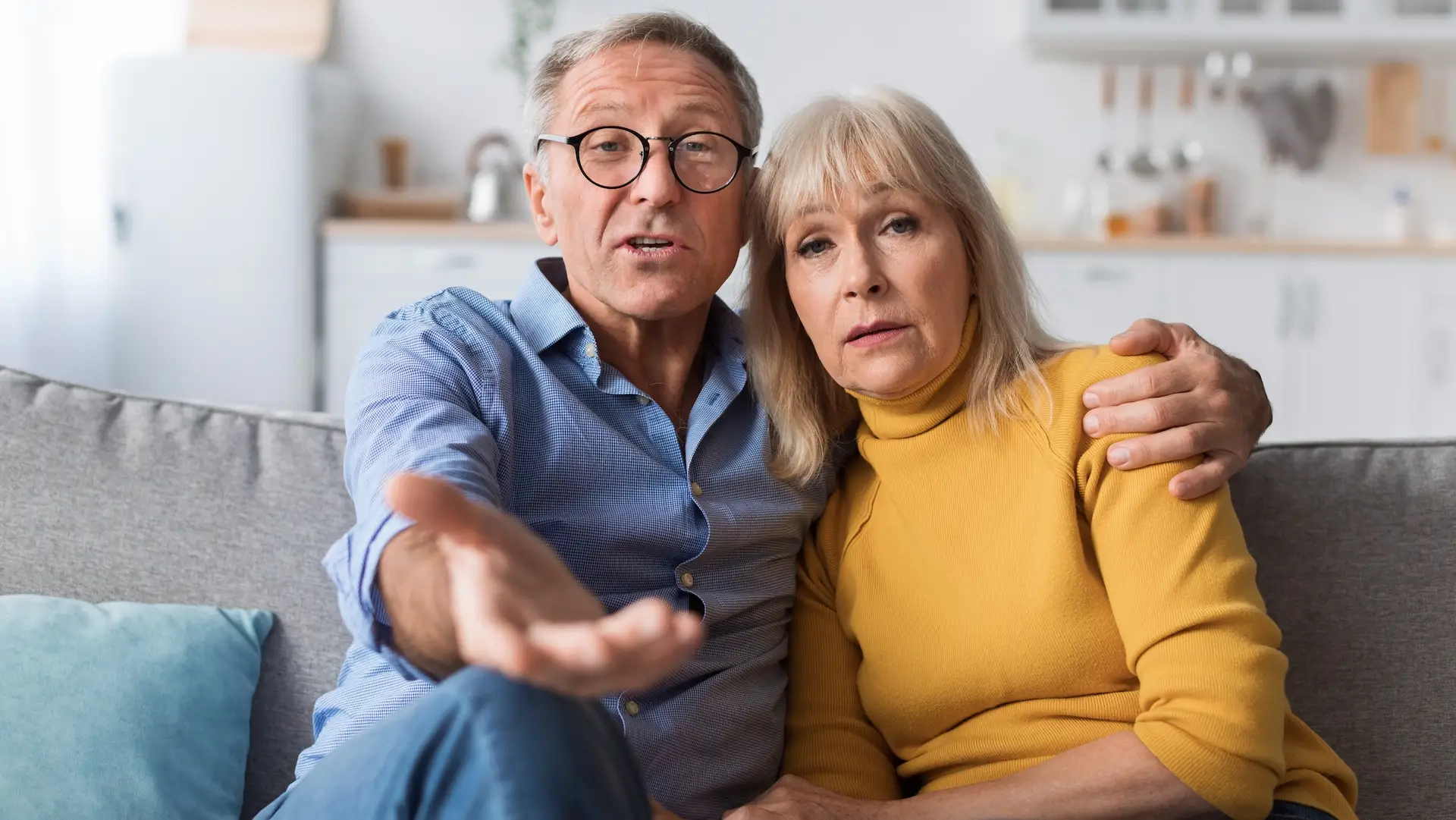 Discontented Senior Couple Talking To Camera Disapproving Criticizing Something Sitting Together On Sofa At Home. Displeased Customers. Communication Problems With Older Parents