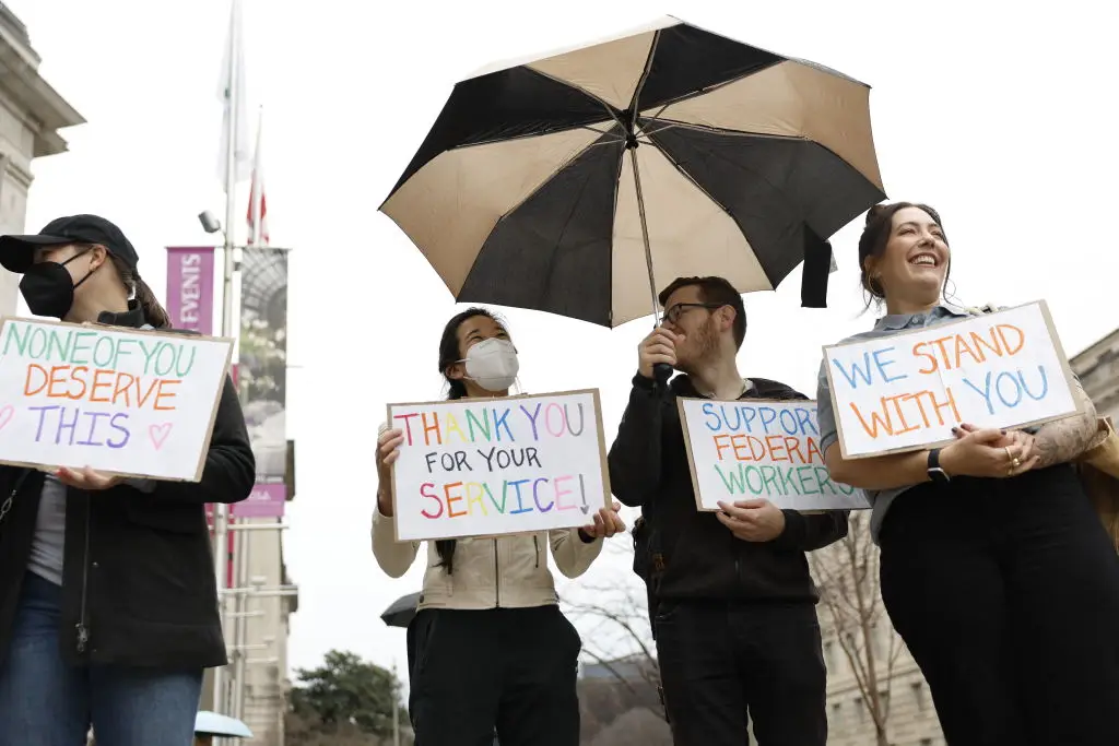 Protestors hold signs as people gather outside the Ronald Reagan Building during a 'clap out' in support of USAID staff that were fired (TING SHEN/AFP via Getty Images)