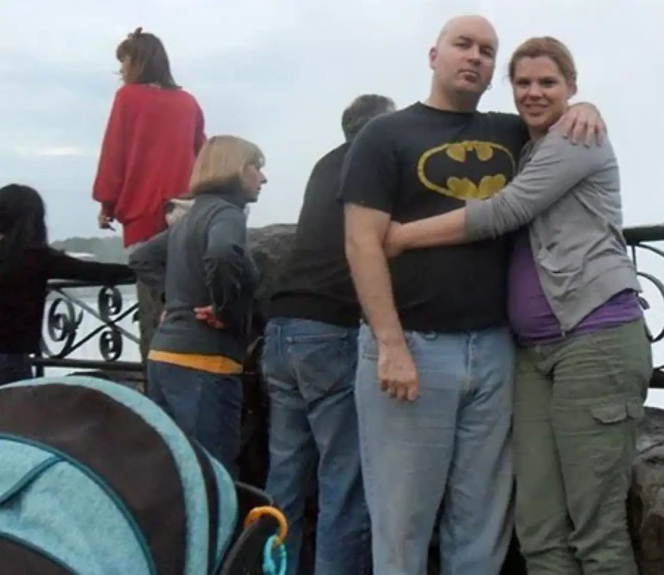 A couple pose for a picture while Tokumasu can be seen straddling the railings behind them in a red jumper. (r/lastimages/Reddit)