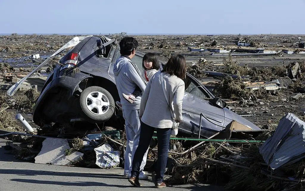 A family looks at a damaged vehicle following a tsunami in the aftermath of a massive 9.0 earthquake in Minamisoma, Fukushima, in March 2011 (KAZUHIRO NOGI/AFP via Getty Images)