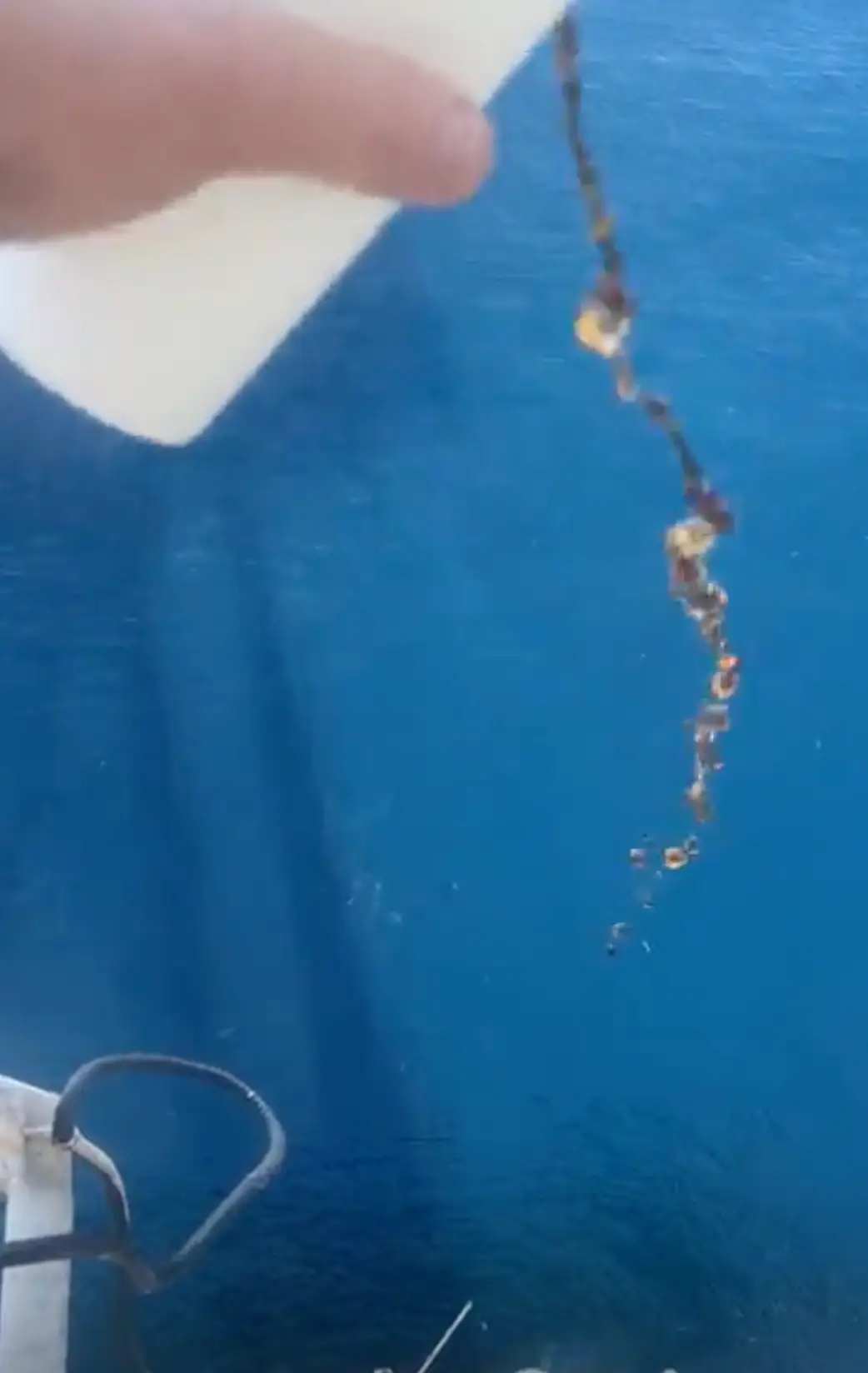 The person pours a drink into the ocean.