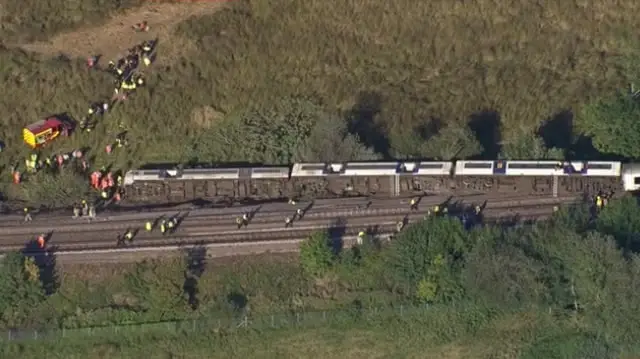 Photographs show the carriages of a train lying on their side.