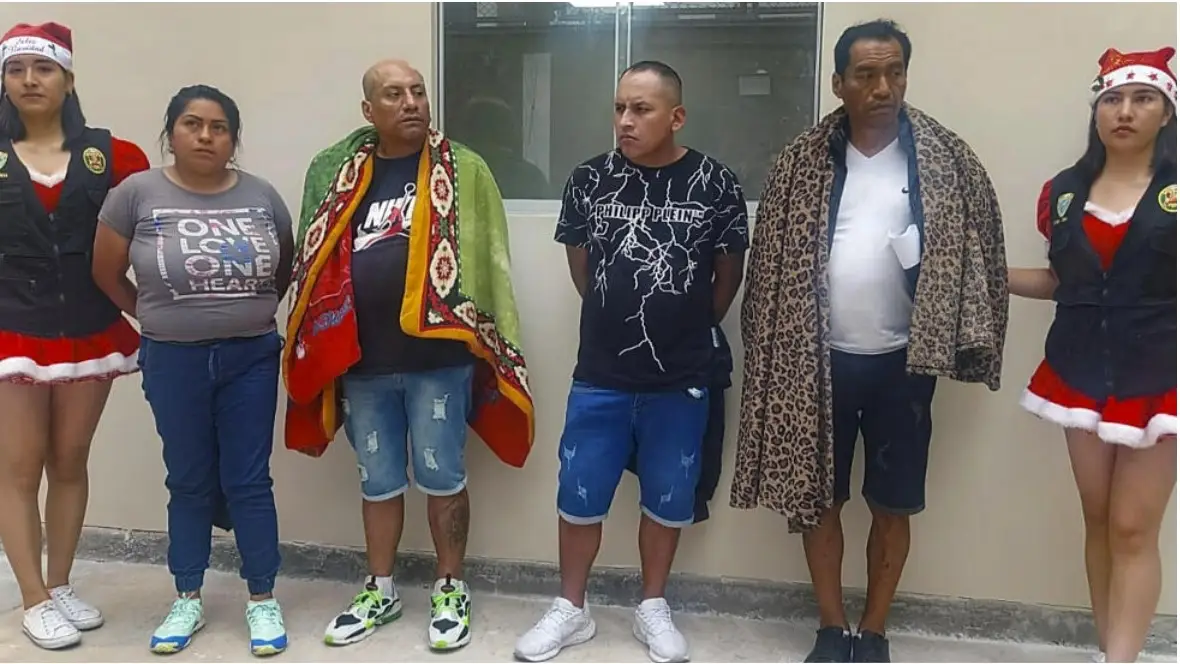 Members of Peru's National Police, dressed in Christmas costumes, stand near four drug suspects.