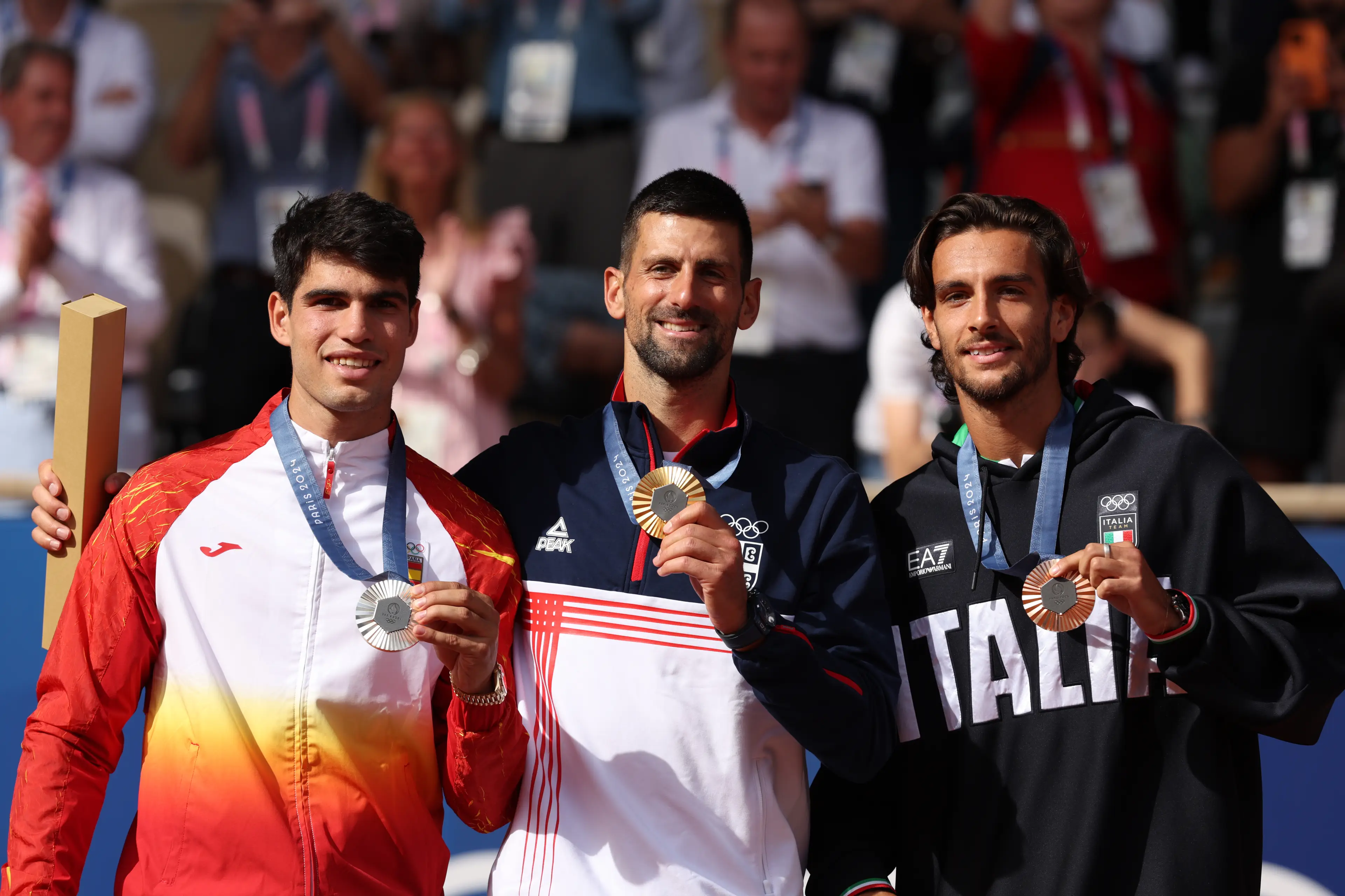 Djokovic and Alcaraz pick up their medals alongside bronze winner Lorenzo Musetti. (Clive Brunskill/Getty Images)