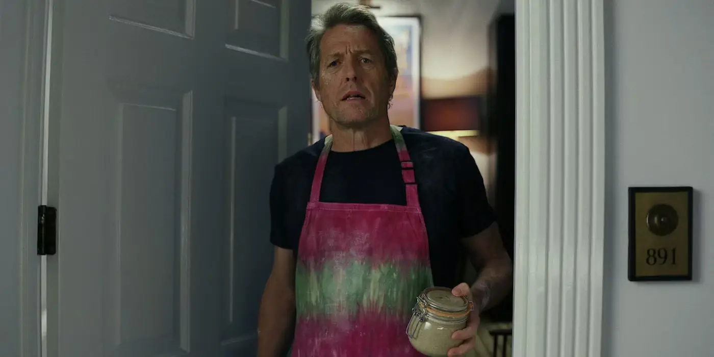 Hugh Grant in Glass Onion, wearing a fetching apron.
